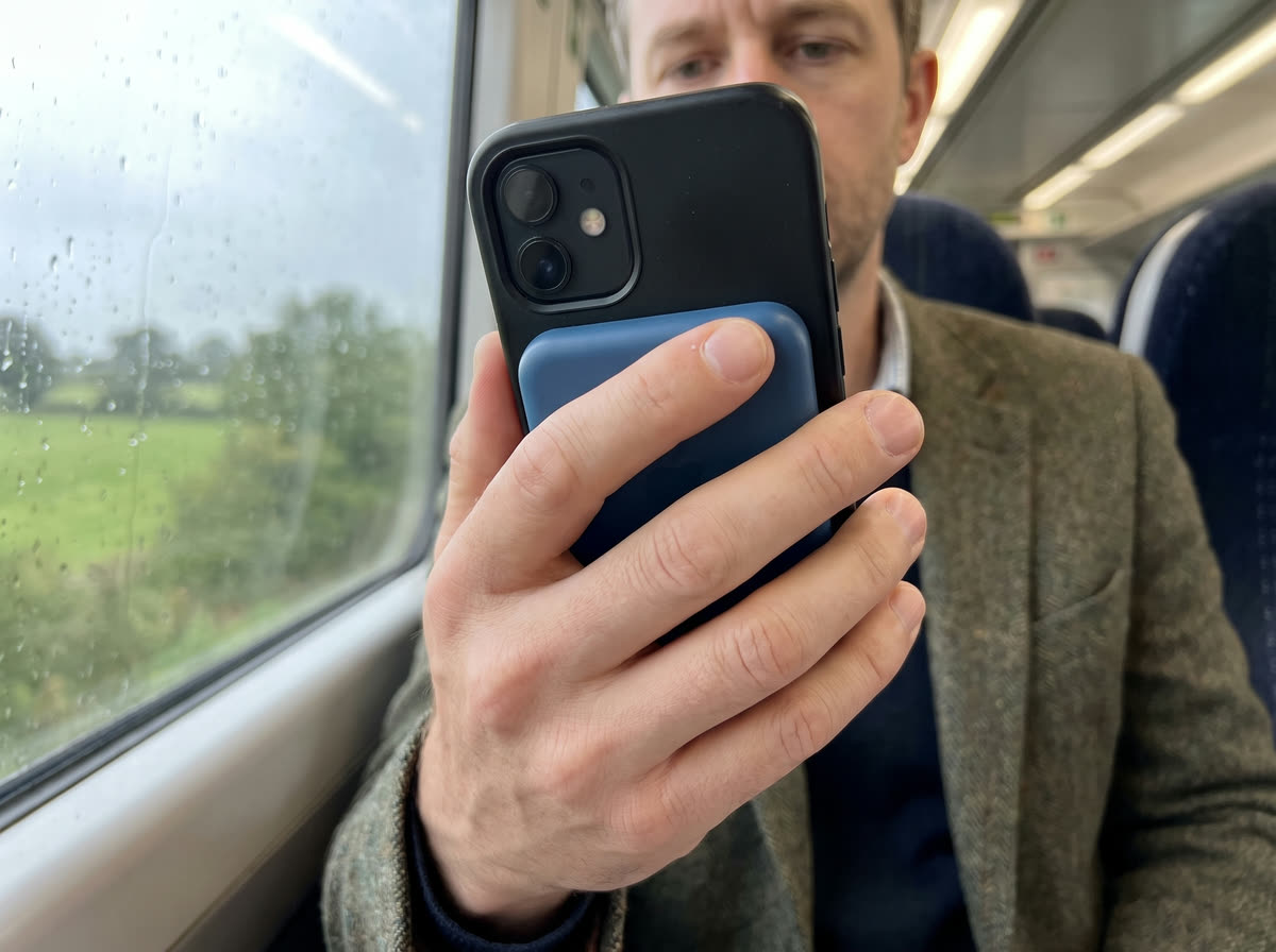 A commuter on a train holding a phone with the royal blue Magnetik power bank attached